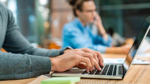 Two people working at shared desk with laptop and phone